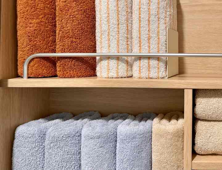 木目調の棚にブラウンとグレーのタオルがきれいに整頓されたミニマルなバスルーム収納空間