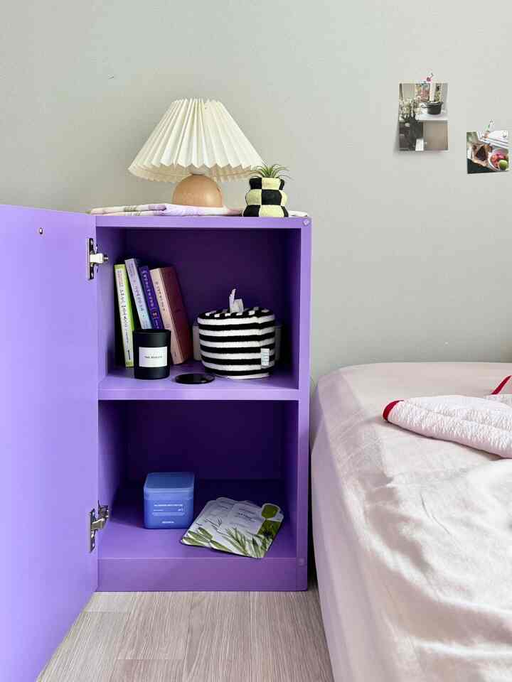 白と紫のトーンの寝室、紫のサイドボードとベッド、照明が調和した清潔感のある空間