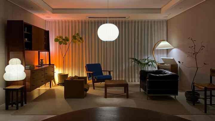 Mid-century modern living room featuring warm wood furniture and sheer white curtains, assorted armchairs with soft lighting creating cozy ambiance