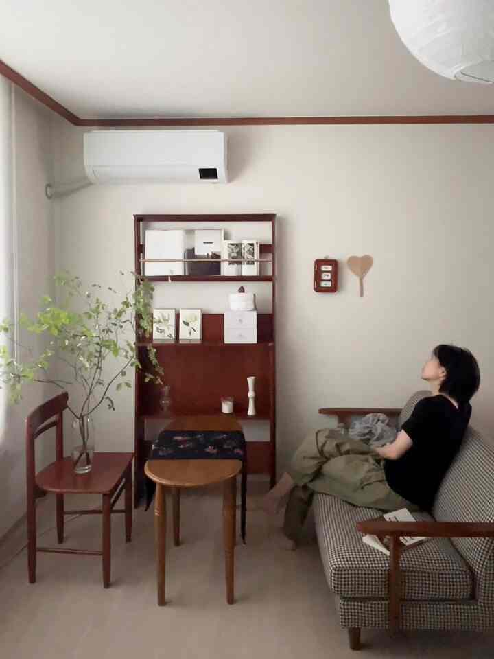 木目調とチェリー巾木が特徴の一人暮らし用リビング、ヴィンテージのソファと本棚が配置された暖かみのある空間