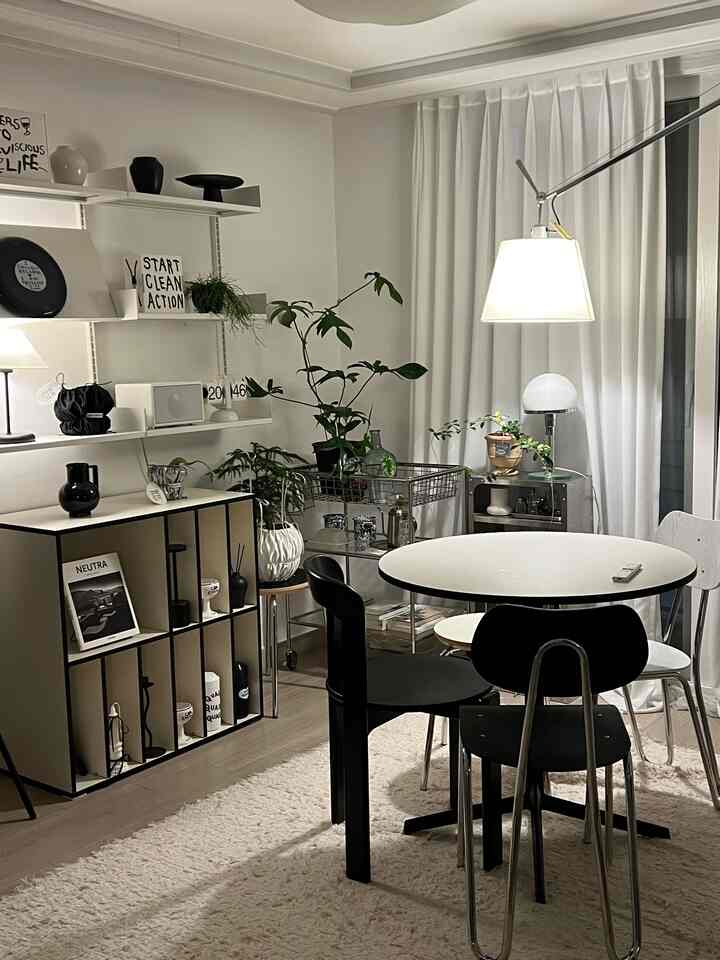白を基調としたダイニングルーム、黒白のダイニングチェアと丸いダイニングテーブル、フロアランプと植物が調和するモダンな空間