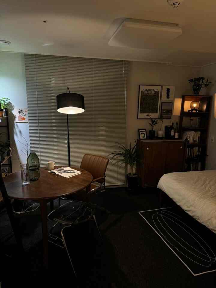 暗めの照明と木製家具、ブラインドがあるナチュラルなワンルームのリビングと寝室空間