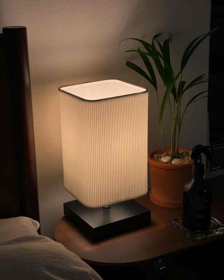 柔らかな白い光のテーブルランプが置かれたブラウンのナイトテーブルと植物が配置された居心地の良い寝室のインテリア