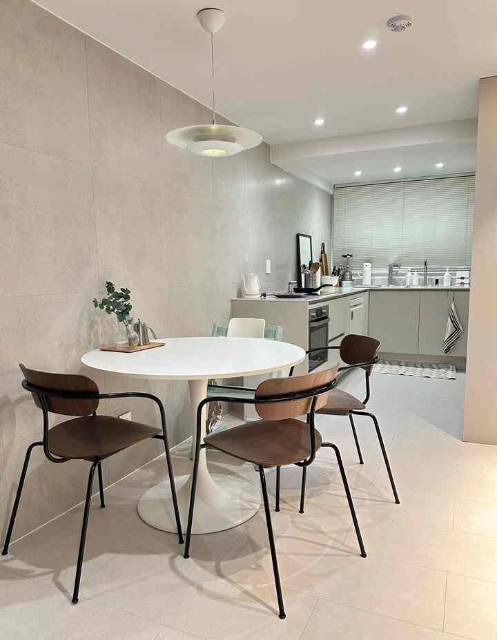 グレーとホワイトのトーンのキッチンとダイニングルーム、丸いダイニングテーブルと木製の椅子が配置されたモダンで清潔感のある空間