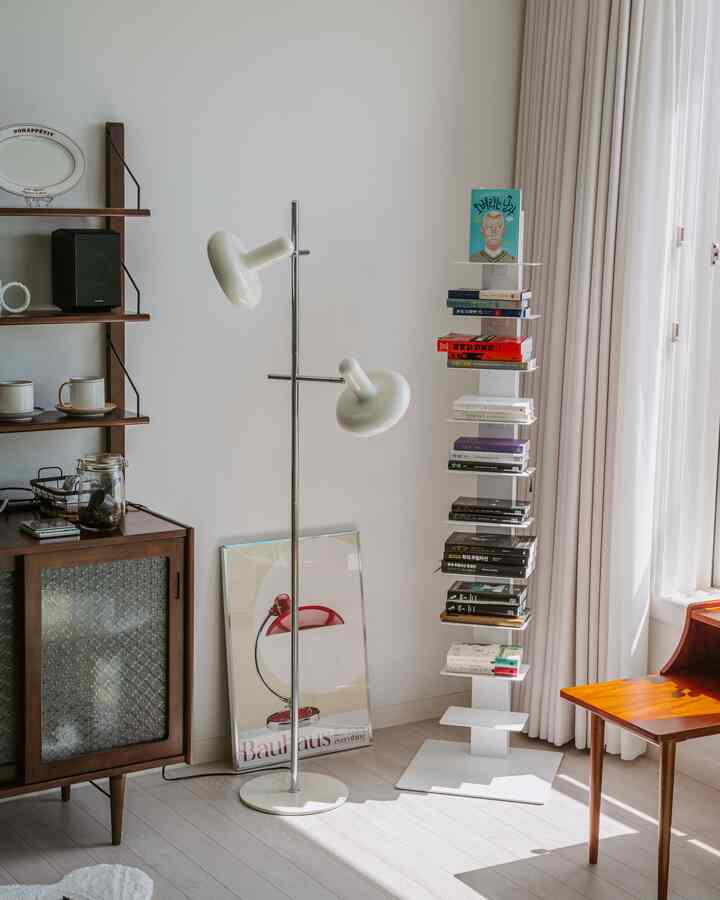 A white and brown toned living room featuring a Mid-Century Modern double light floor lamp and a vertical bookshelf, cozy atmosphere