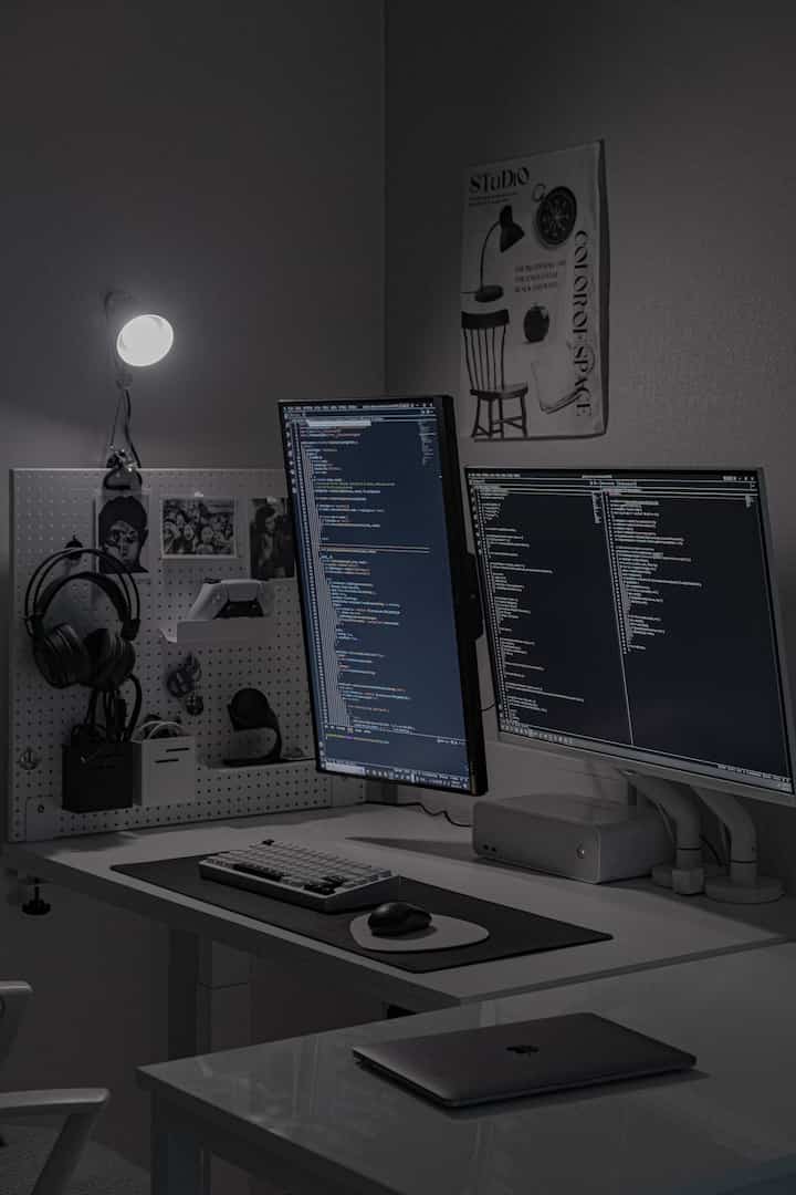 白と黒のトーンのホームオフィスデスク、有孔ボードの収納と2台のモニターを備えたモダンな開発者向けスペース