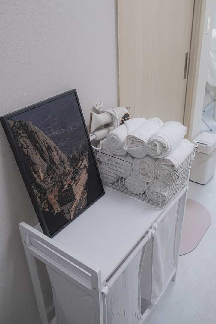 白を基調としたトイレ手前の空間、タオルと洗濯物を収納するワイヤーバスケットとランドリーバスケットが整った清潔感のあるインテリア