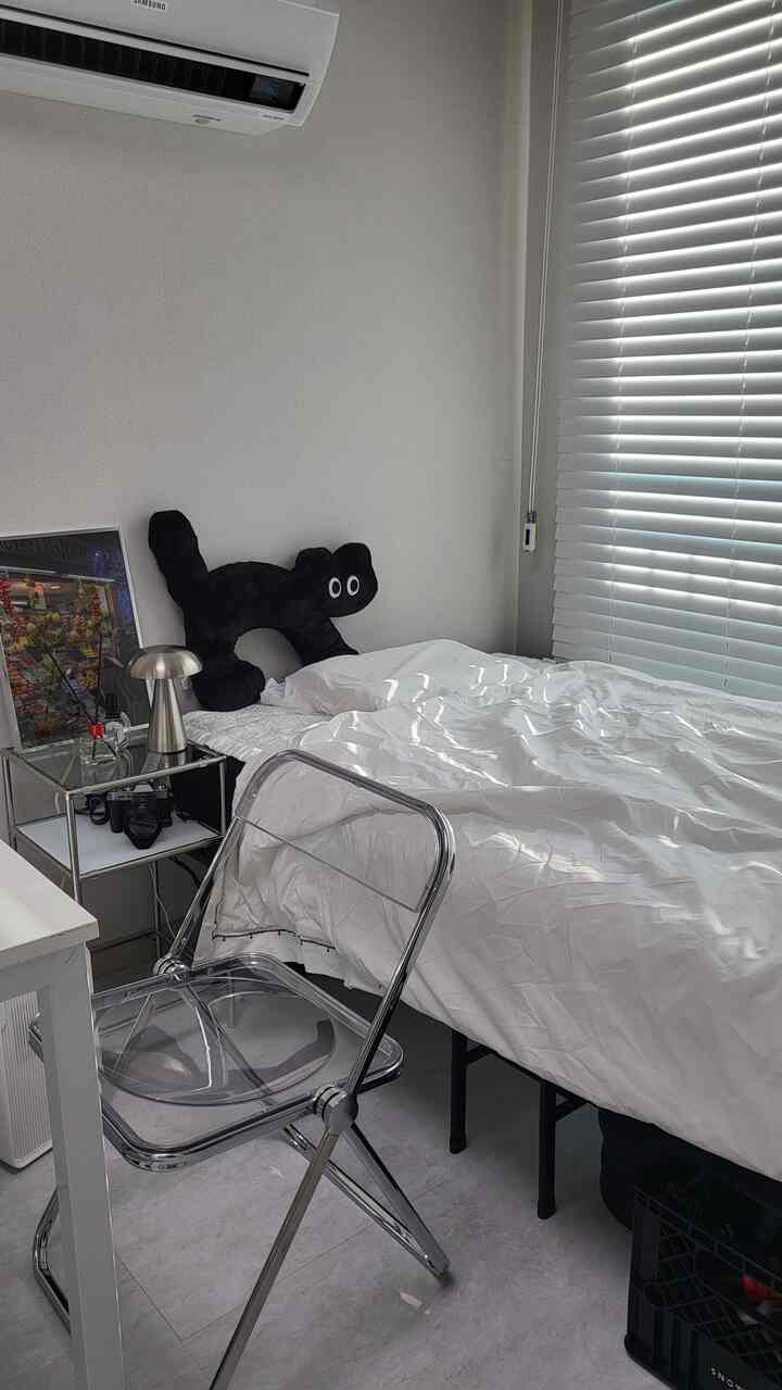 白とシルバーのトーンの寝室、透明な椅子とモジュール棚、ミッドセンチュリースタイルの小物が配置された清潔感のある空間