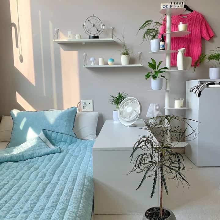 白と青のトーンの寝室、ベッドとナイトテーブルの上にミニファンと植物が配置された清潔で快適な空間