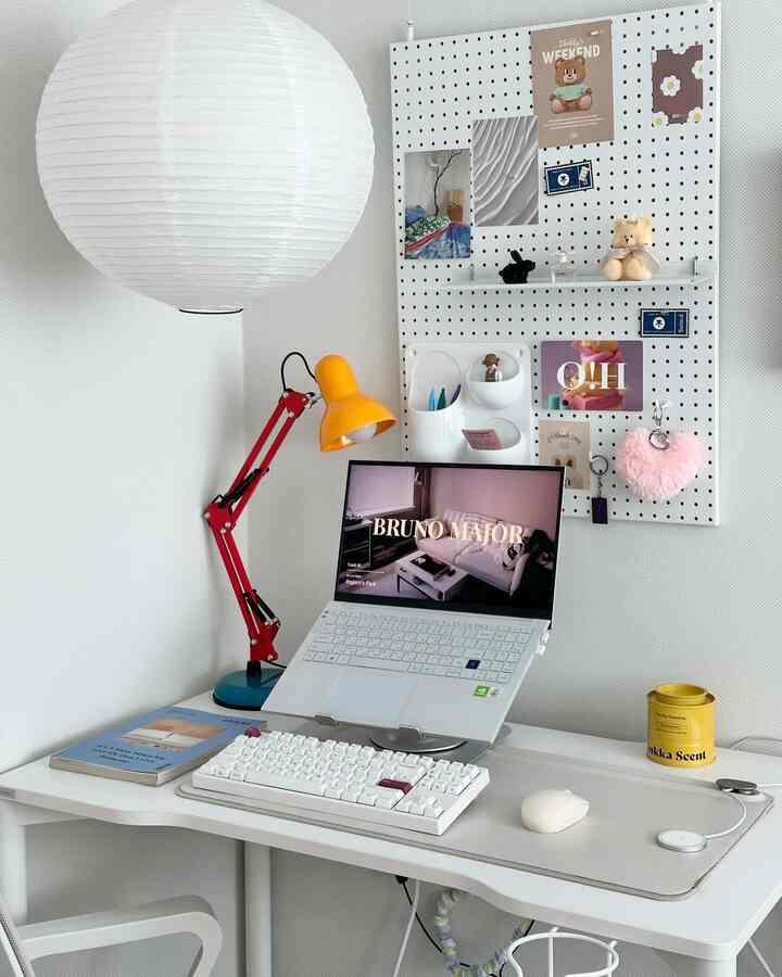 白色のトーンで統一された小さなホームオフィス、ノートパソコンとキーボード、黄色のデスクランプが配置されたシンプルなインテリア