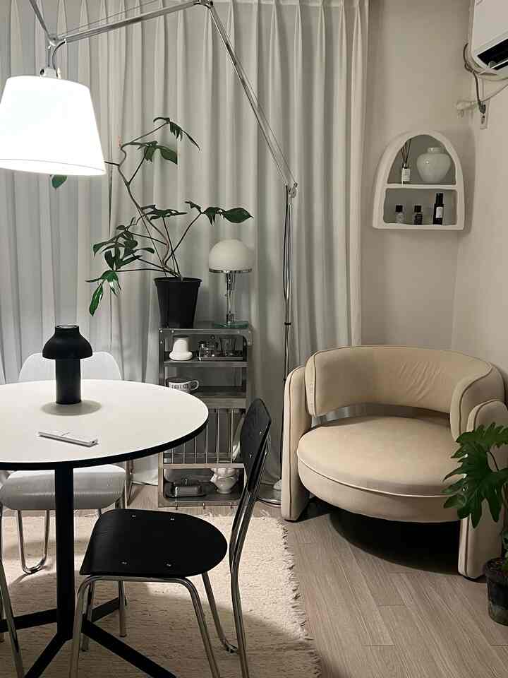 白とベージュのトーンのワンルーム、丸いダイニングテーブルとベージュのアームチェアが配置された、居心地の良いカフェ風のナチュラルモダンなインテリア