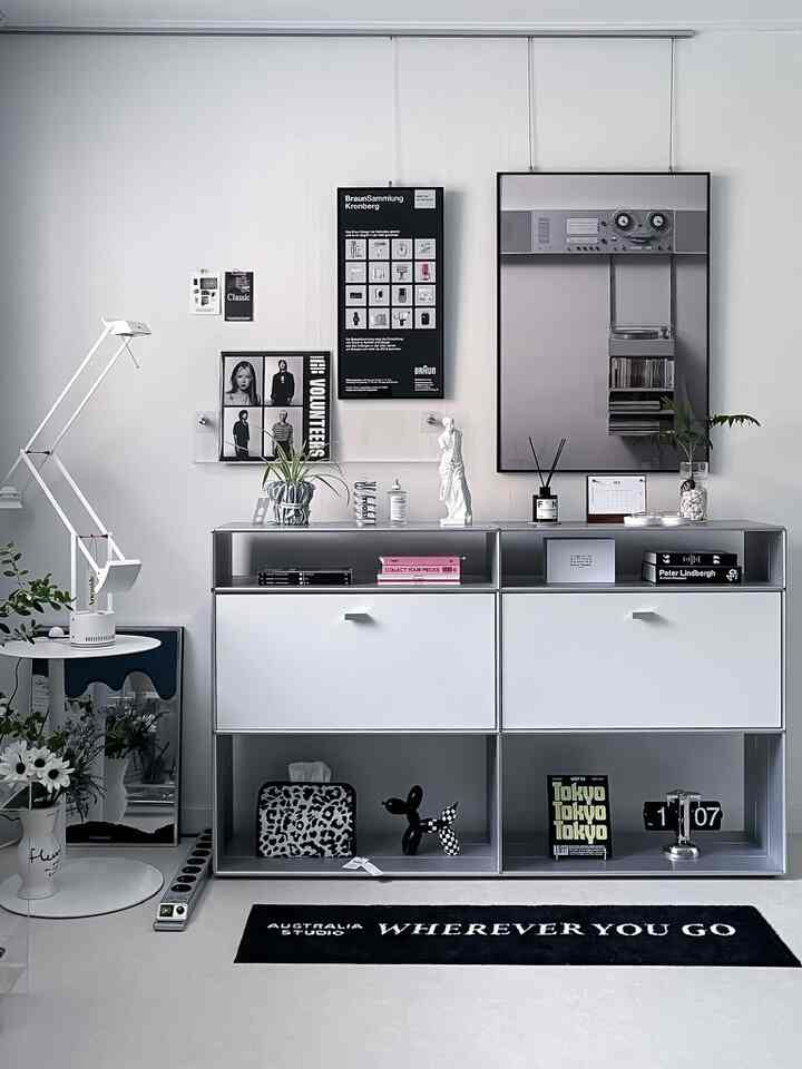 モノトーンのリビングルーム、棚とナイトテーブルにポスターやオブジェが配置されたシンプルなインテリア