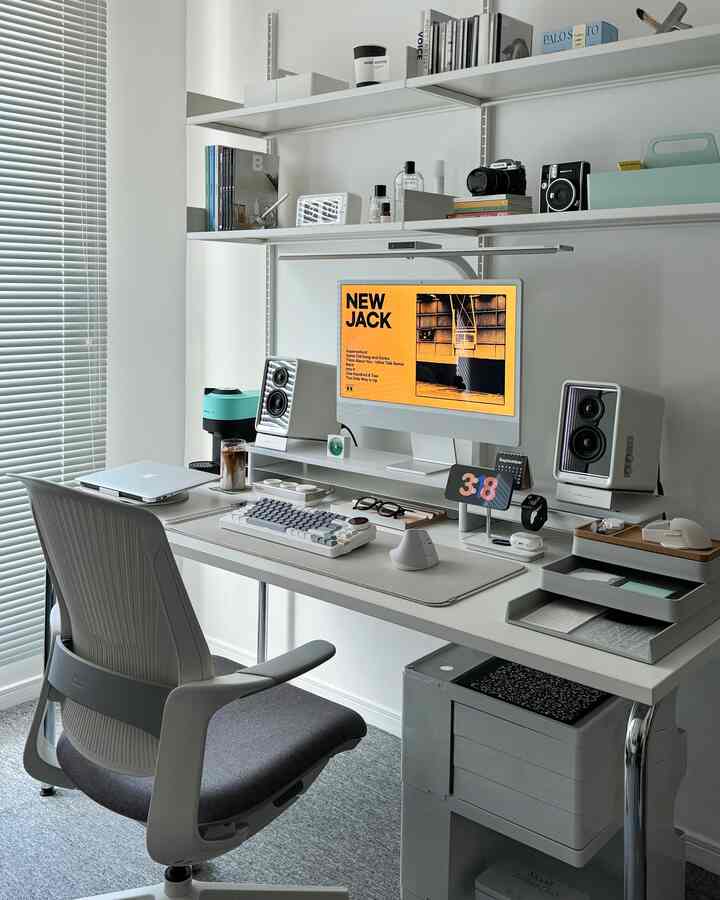 White and gray toned compact home office featuring a central desk with computer monitor and office chair in a modern workspace