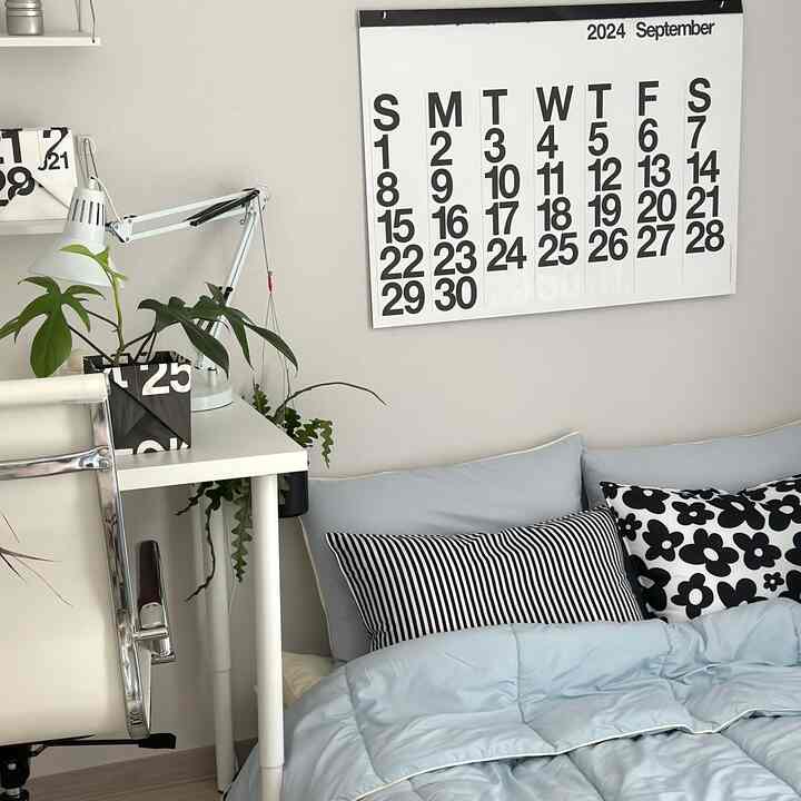 白と淡いブルーの色調の寝室で、整頓されたデスクと柄付きクッションが配置された北欧風の雰囲気のあるインテリア