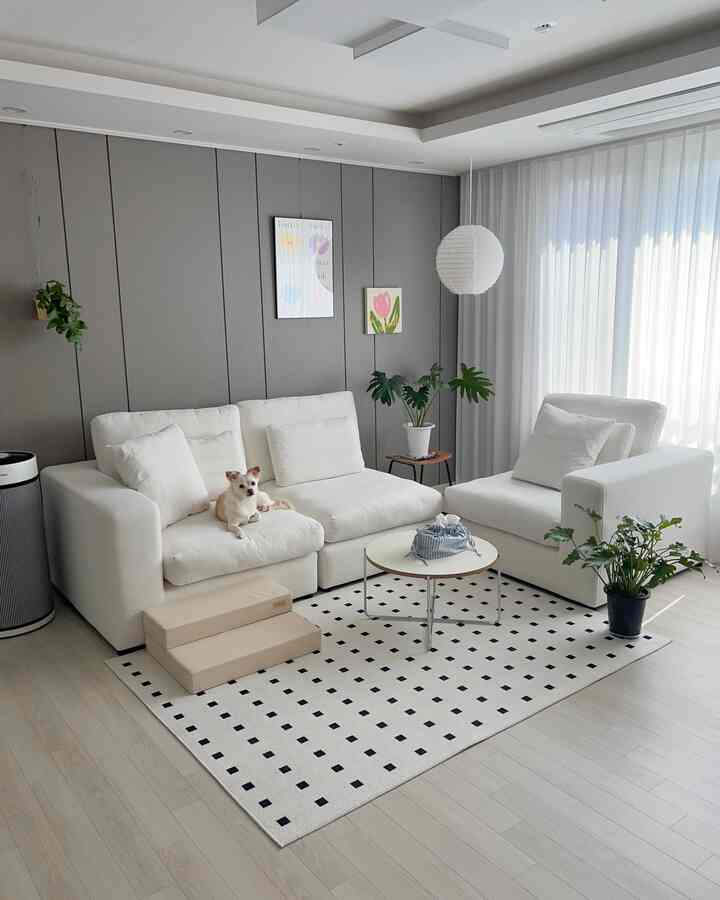 白とベージュのトーンのリビング、モジュラーソファとラグ、植物が配置されたシンプルでナチュラルなインテリア