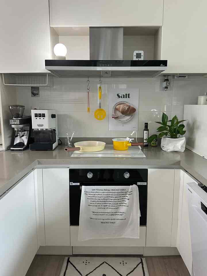 白を基調としたキッチン、IHクッキングヒーターとコーヒーマシン、黄色の調理器具、観葉植物が配置されたモダンで清潔感のある空間