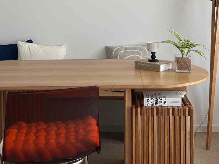 A wood tone and white living dining room featuring a wooden dining table with bench, plant, and lamp creating a simple interior atmosphere