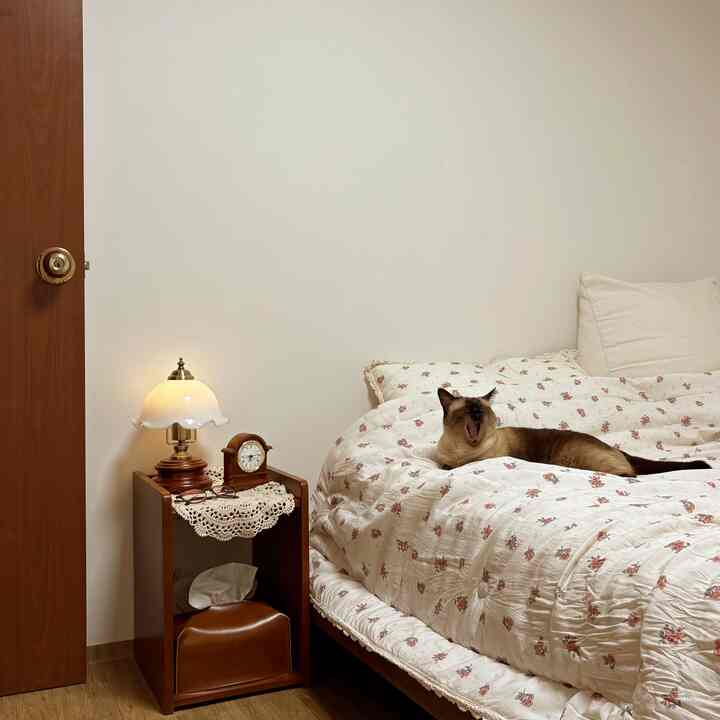 アイボリーと木目調が調和する寝室、花柄の掛け布団の上に猫が横たわる落ち着いた雰囲気のインテリア