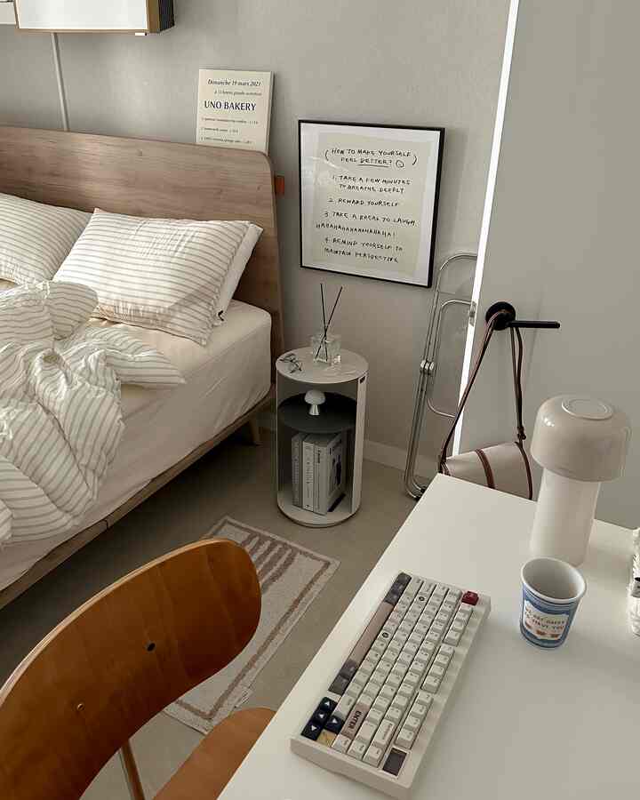 ホワイトとウッドトーンの寝室、ミニマルなナイトテーブルとデスクが配置された落ち着いた印象の空間