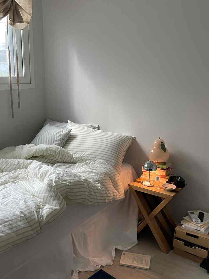 A simple and cozy white and wood-tone bedroom featuring striped bedding and a small table lamp on the wooden nightstand.