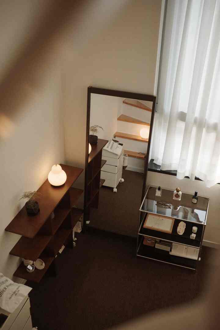 柔らかなベージュ調の狭い部屋、大きな全身鏡と木製棚、白いシアーカーテンが配置された雰囲気のある空間