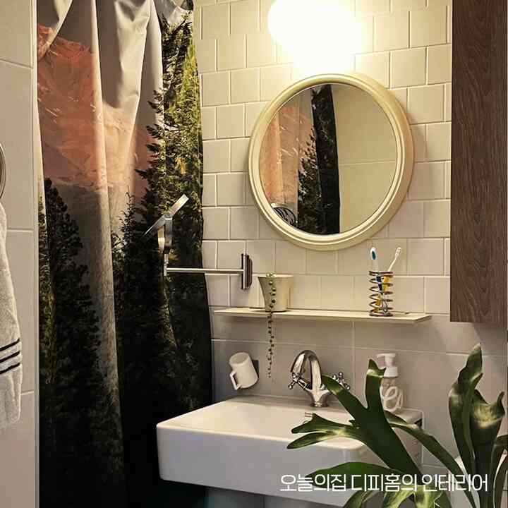 白いタイル壁と丸い鏡、森の柄のシャワーカーテンが配置された清潔感のあるバスルーム