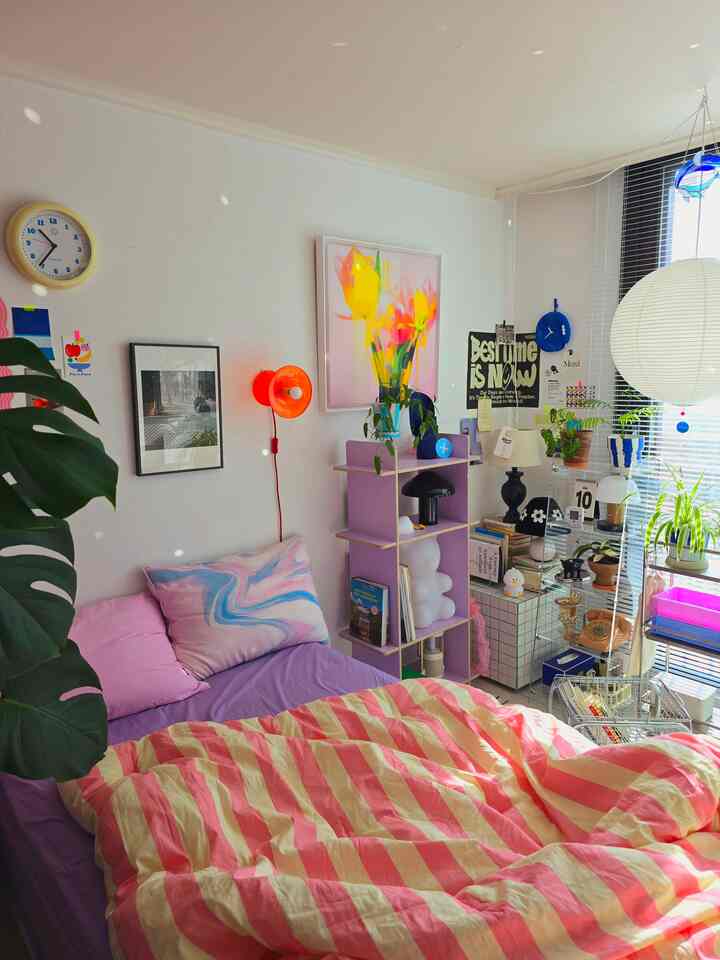 白い壁とピンクの寝具が特徴の6畳の寝室、ベッド横に棚と植物が配置された雰囲気のあるインテリア