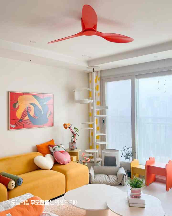イエローとレッドのトーンが特徴的な、黄色いソファと赤いシーリングファンが置かれた明るくモダンなリビングルーム