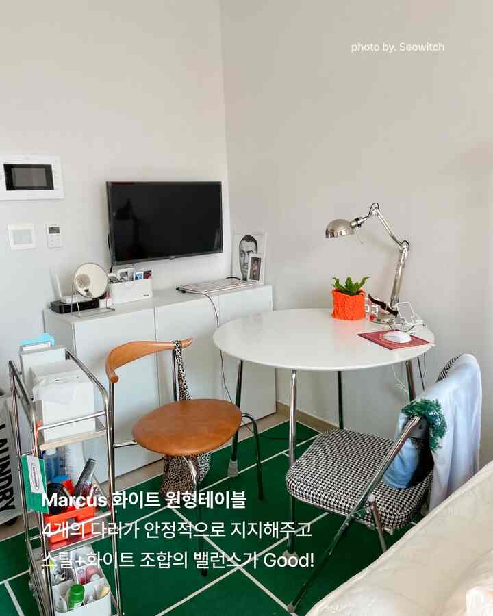 白と緑のトーンの小さな部屋、円形の白いテーブルと多様な椅子が配置されたミニマルな空間