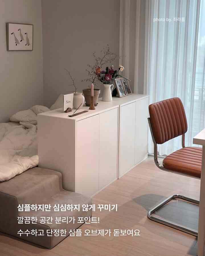 やわらかなベージュとホワイトのトーンが特徴のナチュラルスタイル寝室。白い収納キャビネットとブラウンのアームチェアが配置された清潔感のあるシンプルなインテリア