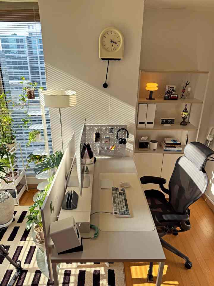 白と木目調が調和したワークスペース、広いデスクと収納アクセサリー、多くの植物が配置された居心地の良いホームオフィス