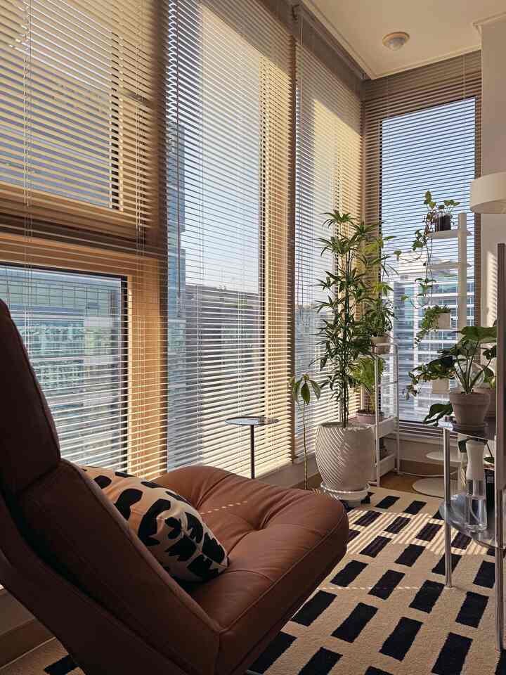 ナチュラルな木目調とブラインドがある小さなバルコニー空間、ラウンジチェアと植物が落ち着いた休息を演出するインテリア