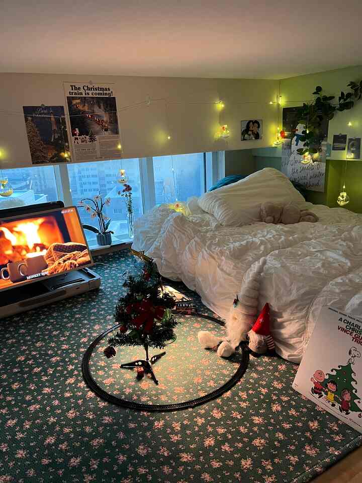 グリーンのフローラルカーペットと白い寝具が配置されたロフト寝室、クリスマス装飾とストリングライトが雰囲気のある空間を演出