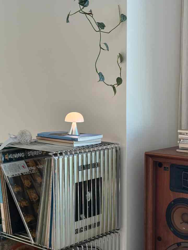 Modern space with white walls featuring a metal rack holding vinyl records and a small portable mushroom-shaped LED lamp on top