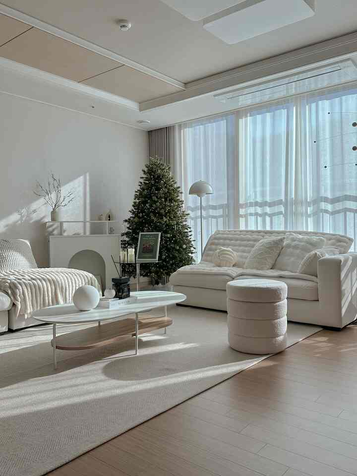 Bright white and beige toned living room featuring a Christmas tree, sofas, and coffee table with a warm, clean atmosphere