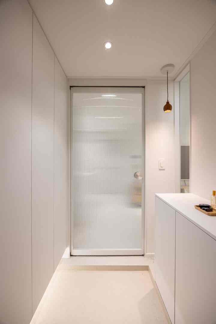 ホワイトトーンの清潔感ある玄関、透明なリブガラスドアと大きな収納キャビネットが配置されたミニマルモダンなインテリア
