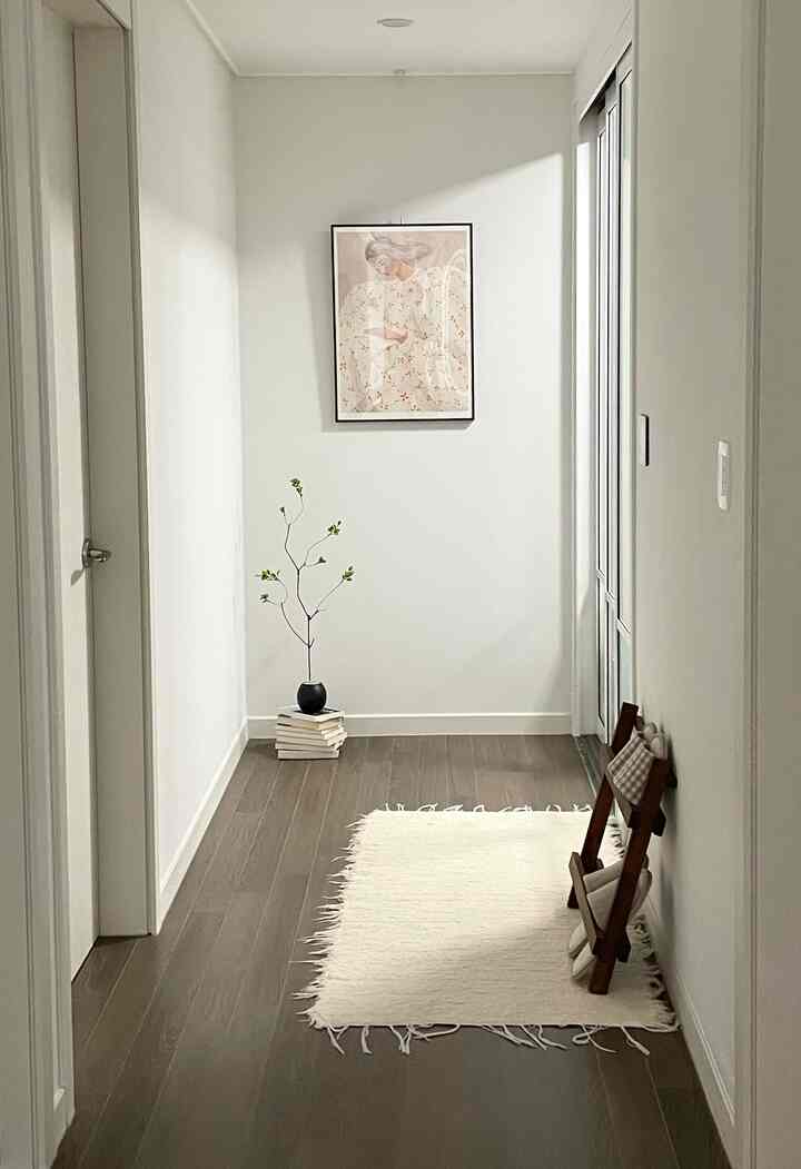 白い壁と茶色の木製床の廊下、ラグと額縁が配置されたナチュラルで落ち着いた雰囲気の空間