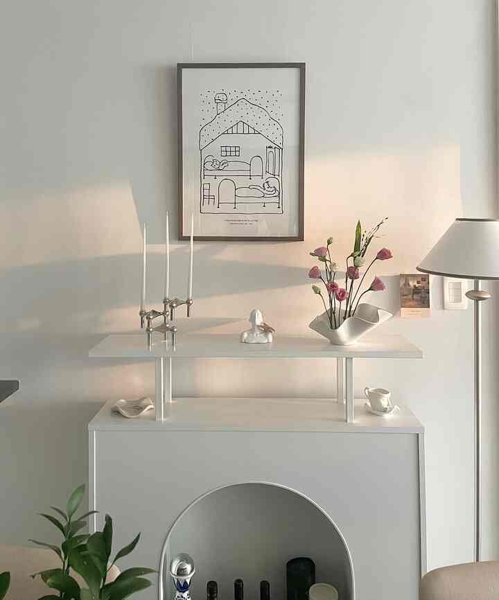 白を基調としたリビング、暖炉コンソールにキャンドルホルダーや花瓶、額縁が配置されたモダンで自然な雰囲気のインテリア