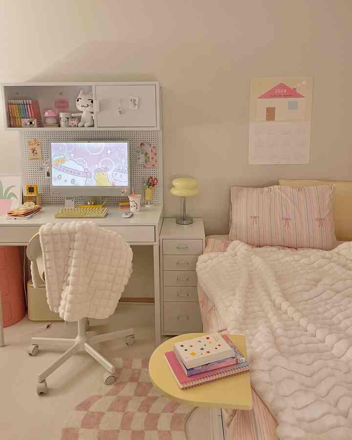 ホワイトとイエローのトーンが特徴のコンパクトな寝室、コンピューターデスクとヘッドボードなしのイエローベッドフレーム、暖かい雰囲気の厚手のブランケットとカレンダーポスターが配置された印象的な空間