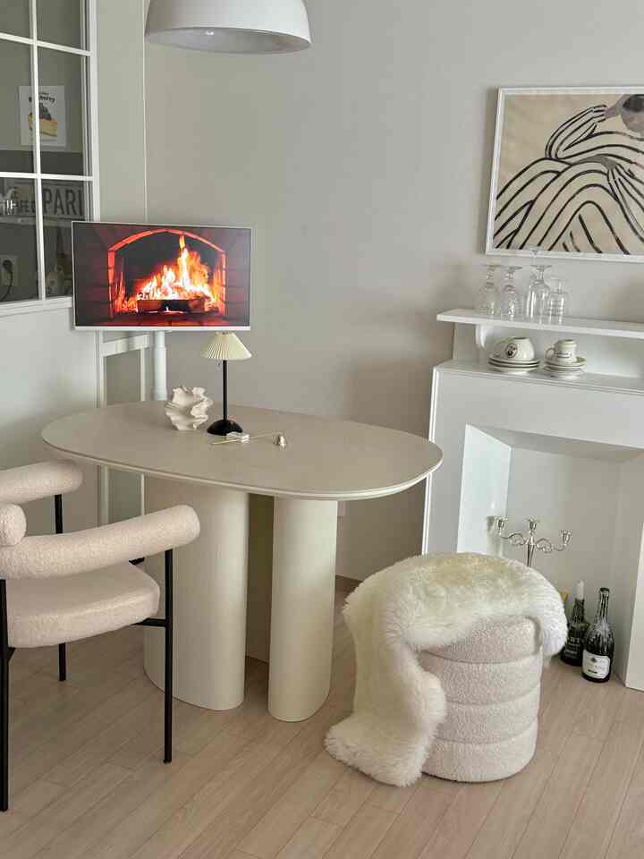 アイボリーとホワイトの色調のリビング、ブークレスツールと楕円形のテーブル、壁暖炉コンソールが配置されたシンプルモダンな空間