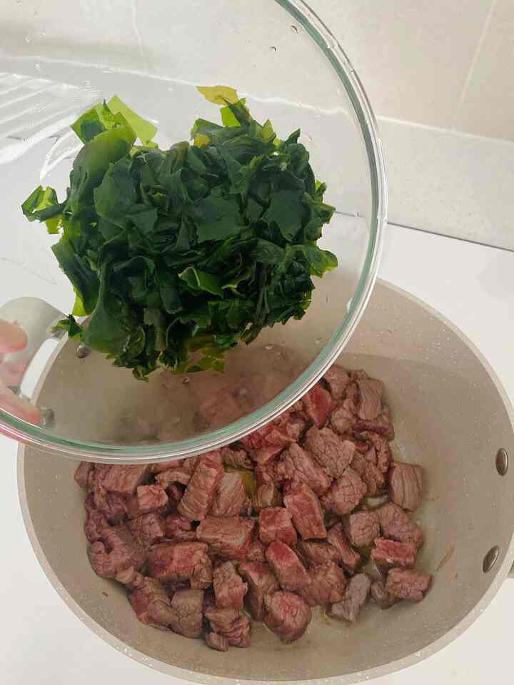 ベージュ色の鍋と透明なガラスボウルに入った緑色の海藻が配置されたキッチンの調理風景