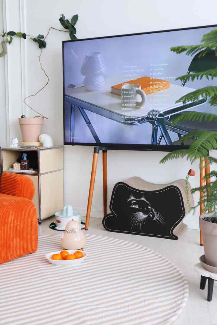 Beige round rug and orange sofa in living room featuring TV stand and cat scratching board with cozy atmosphere