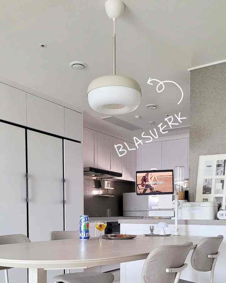 白とグレーのトーンのキッチンとダイニング、シンプルなペンダントライトとモダンな家具が配置された印象的な空間