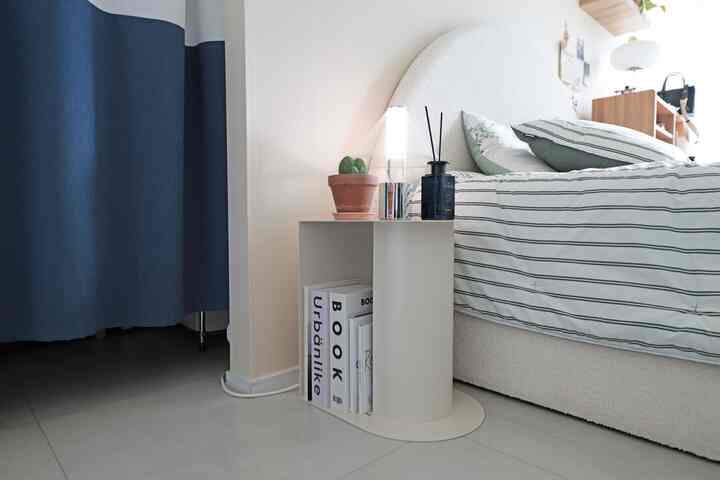 白とネイビーの色調の寝室、ベッドとナイトテーブルに植物や本が配置された雰囲気のあるインテリア