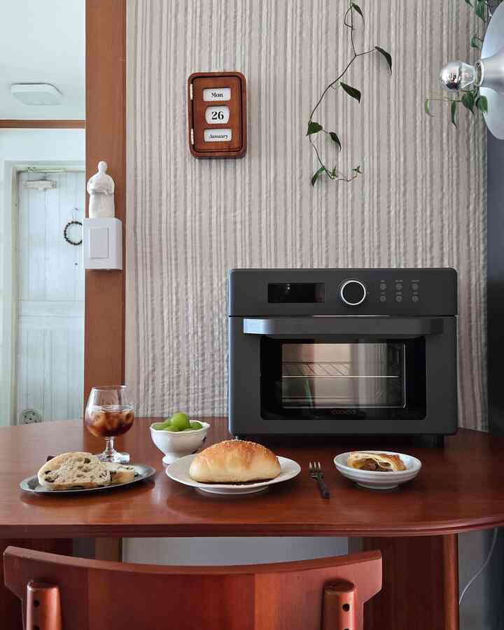 ナチュラルなブラウンの木目調ダイニングルーム、食卓にオーブンとホームカフェセットが配置された雰囲気のある空間