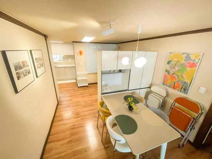 温かみのあるウッドトーンの床と明るいホワイトの家具が調和した居心地の良いキッチン、4人用のダイニングテーブルと壁アートが配置された空間