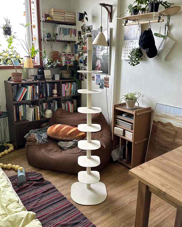 ナチュラルカラーと木目調の小さなリビング、ブラウンのビーズクッション、本棚、キャットタワーが配置された落ち着いた空間