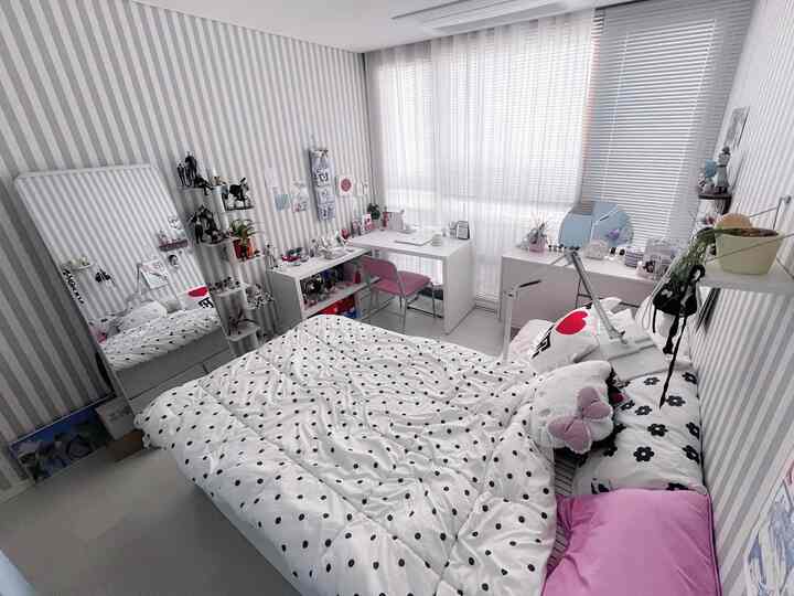 ホワイトとピンクの色調の寝室、中央にベッドとデスク、壁に棚とカーテンが配置されたモダンで落ち着いた空間