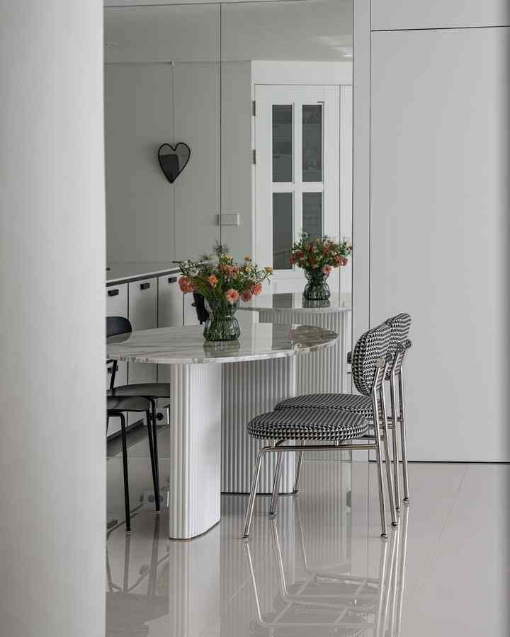A modern kitchen and dining area in white and black tones featuring a marble dining table with a vase of flowers, creating a clean and spacious atmosphere