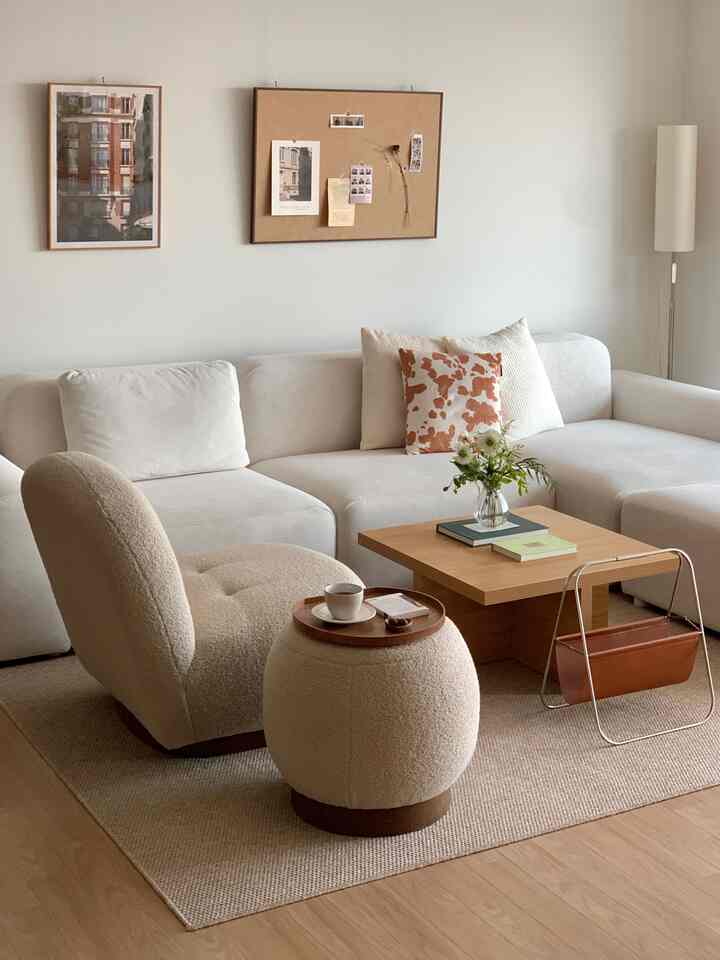 Beige and wood tone living room featuring cream sofa, rounded pouf, and wooden coffee table creating a cozy cafe-style space